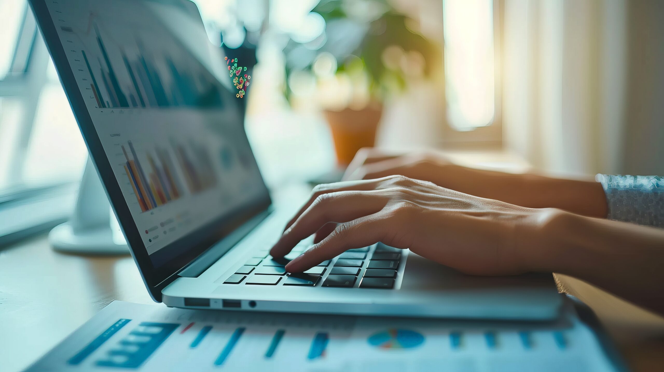 Person typing on a laptop with charts and graphs on screen, representing data analysis and productivity in a business environment.